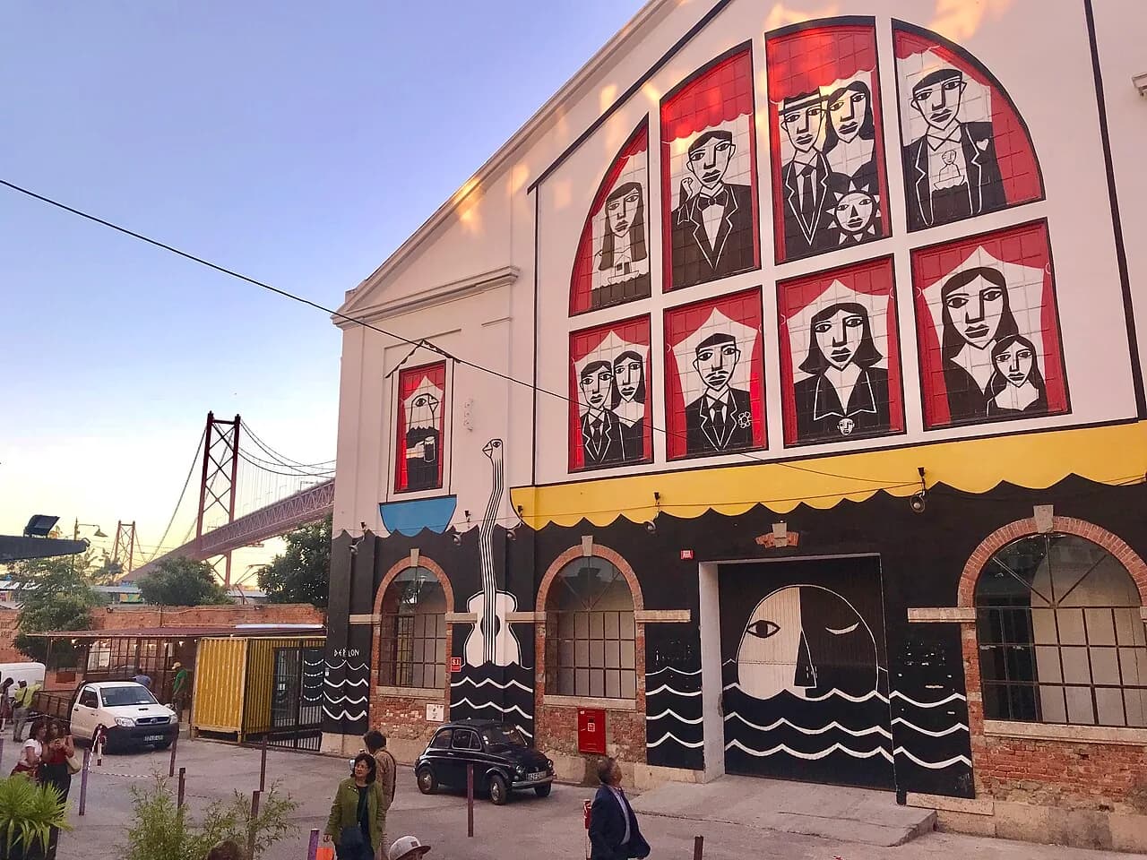 Converted warehouse with a mural facade at LX Factory in Lisbon, with the 25 de Abril bridge behind